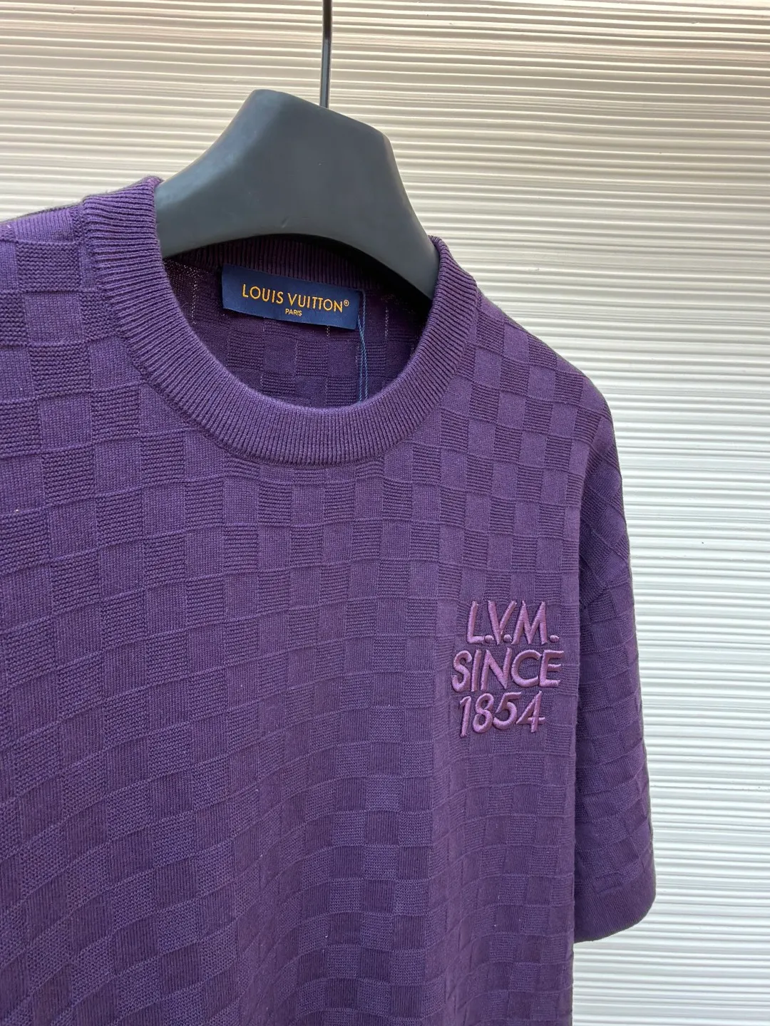 LOUIS VUITTON letter embroidered dark checkerboard jacquard short sleeves ●Original version: Purchased and developed at 9350 ●Item number: 1682319-B00 ●Fabric: 100% cotton ●Technology: jacquard knitting ●Color: Purple ●Version: Fitted version ●Weight: about 340 grams ●Size: S-M-L-XL ●Description: This Louis Vuitton purple knitted short-sleeve is made of custom worsted wool blended fabric. It is created with an 18-needle high-density weaving process using a computerized flat knitting machine to create a three-dimensional checkerboard texture. The checkered pattern is laser positioned and patterned. The size and spacing of each grid are accurate to 0.1 cm, showing a regular relief texture. The left chest uses same-color inlay embroidery technology, and the "LVM SINCE 1854" logo is embroidered with a high density of 1200 stitches/square centimeter. The embroidery thread is made of high-elastic mercerized cotton thread of the same color as the body, forming a natural texture layer with the knitted base. The neckline adopts seamless cylindrical rib technology, which is not easy to loose after high-temperature shaping treatment. The shoulders are made of seamless bonding technology to reduce the abruptness of the seams. The overall micro-profile tailoring combined with the invisible stitching technology of the side seams not only ensures the comfort of wearing, but also makes the body lines smoother. Each process has undergone multiple quality control tests by the brand to ensure the quality and durability of the craftsmanship. The overall wiring is straight and delicate, the fabric is comfortable and soft, and the color is consistent without color difference. It can be matched with the same style to create a fashionable look and control various occasions. Customized accessories, complete with three standards, same style for men and women!